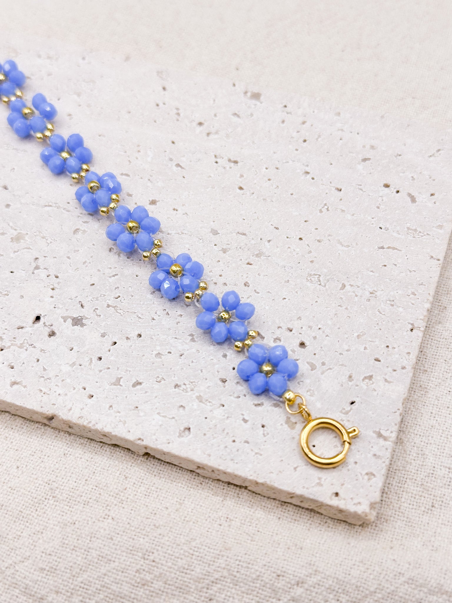 Flora gold bracelet with blue flower-shaped beads showing clasp over stone background