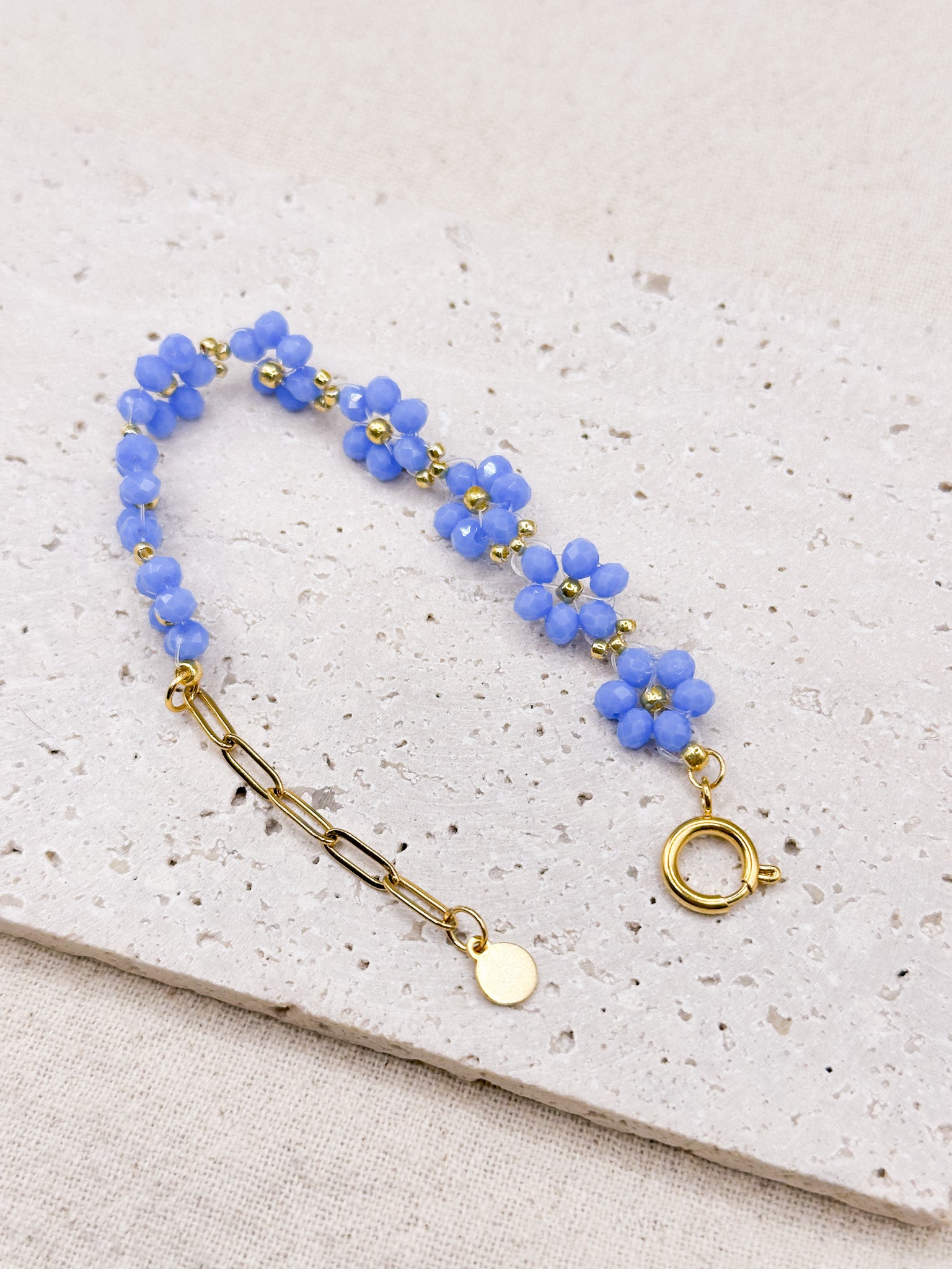 Flora gold bracelet with blue flower-shaped beads curved over stone background