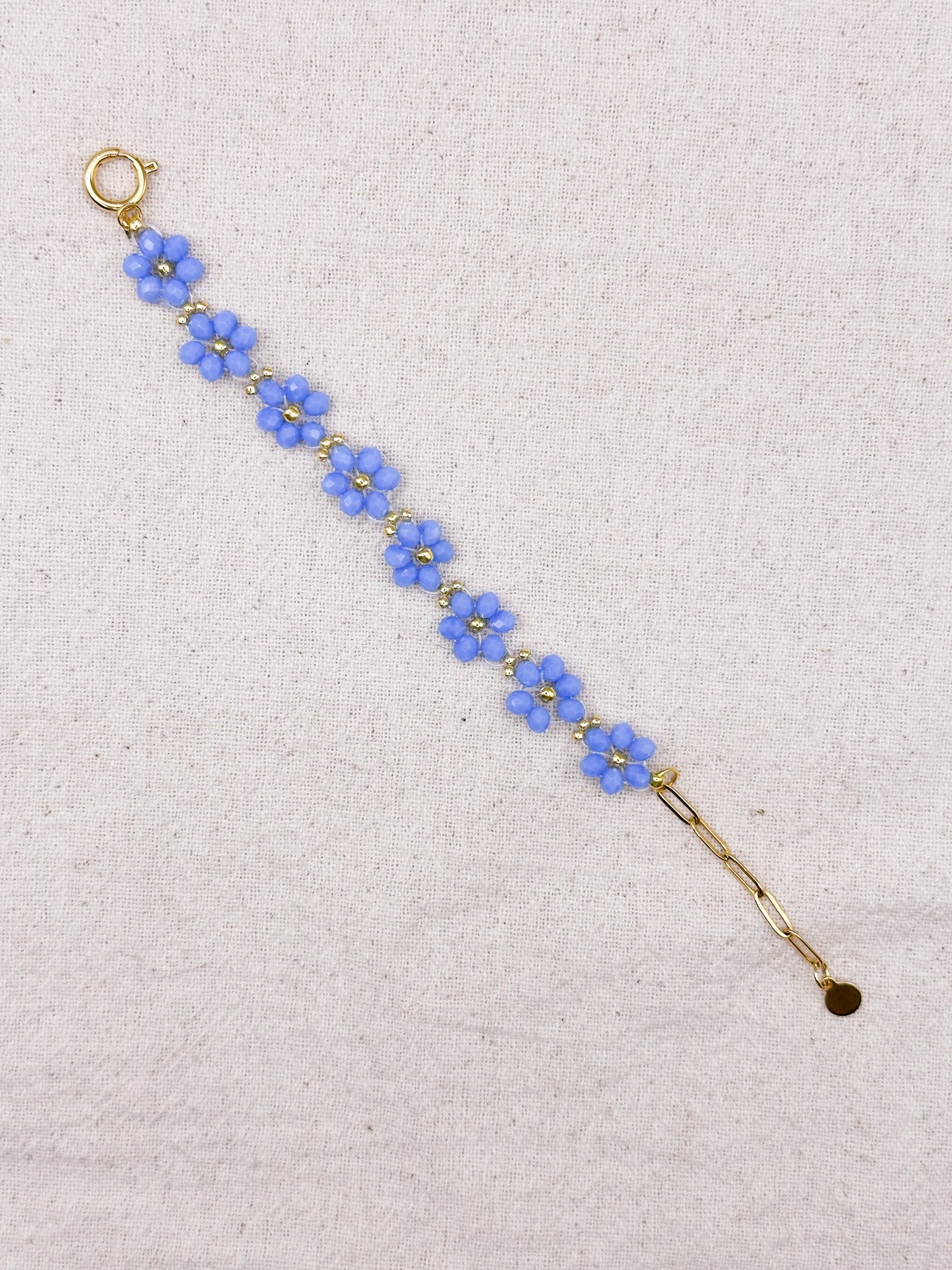 Flora gold bracelet with blue flower-shaped beads over textile background